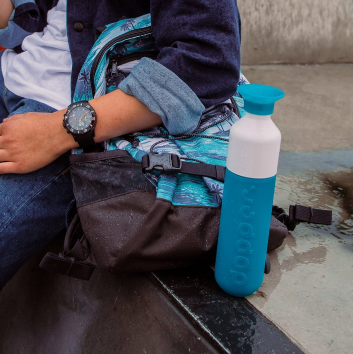 Person sitting with a backpack and blue water bottle on a concrete surface