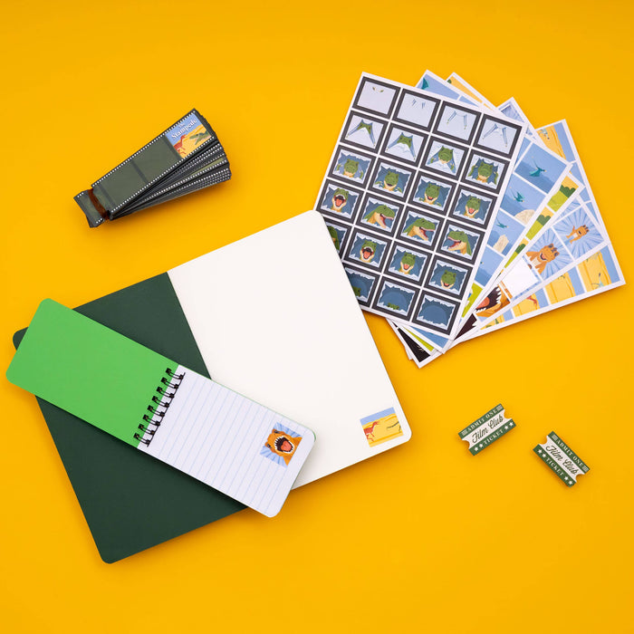 A flat-lay arrangement of sticker sheets, a small spiral notebook with a green cover, and several small rectangular sticker packs on a solid yellow background.