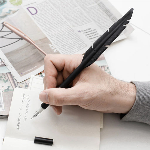hand holding a black silicone feather pen writing important notes artfully  surrounded by newspapers
