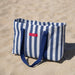 Blue and white striped tote bag with a red label on sand