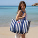 Woman holding a blue and white striped tote bag on a beach