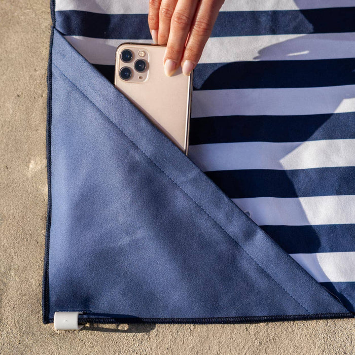 Hand inserting a phone into a pocket on a blue and white striped towel with a sand background