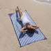 Person lying on a blue and white striped beach towel at the beach.