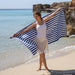 Woman holding a striped towel on a beach with ocean and rocks in the background