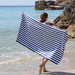 Person holding a blue and white striped towel on a beach with rocks and ocean in the background