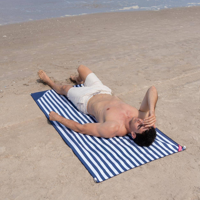 Man lying on a blue and white striped towel on a sandy beach.