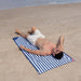 Man lying on a blue and white striped towel on a sandy beach.