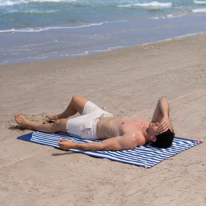 Man lying on a striped beach towel at the beach with ocean waves in the background
