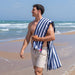 Man on a beach with a blue and white striped towel draped over his shoulder