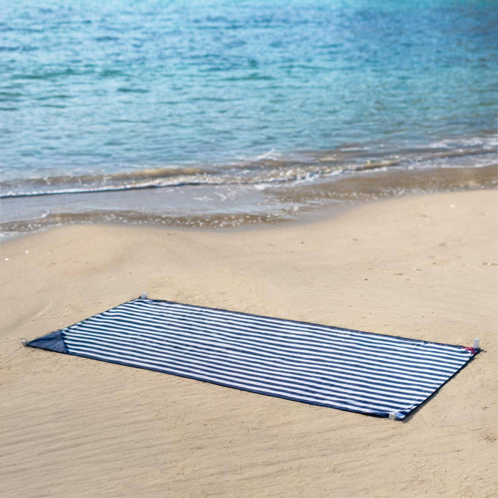 Navy and white striped towel on a sandy beach with ocean in the background