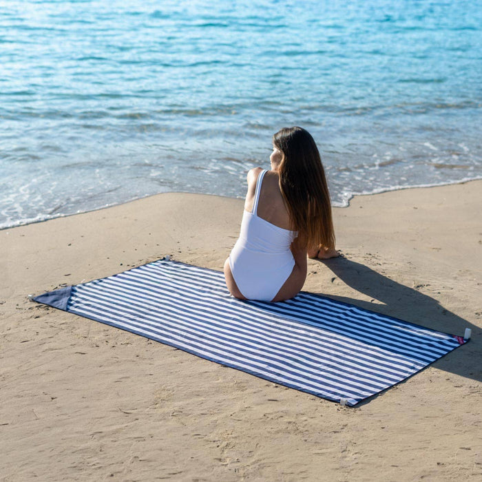 Woman sitting on a blue and white striped beach towel by the ocean