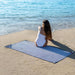Woman sitting on a blue and white striped beach towel by the ocean