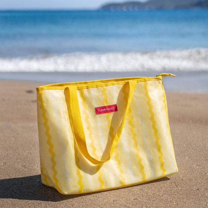 Yellow striped cooler bag on a sandy beach with ocean in the background