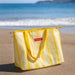 Yellow striped cooler bag on a sandy beach with ocean in the background
