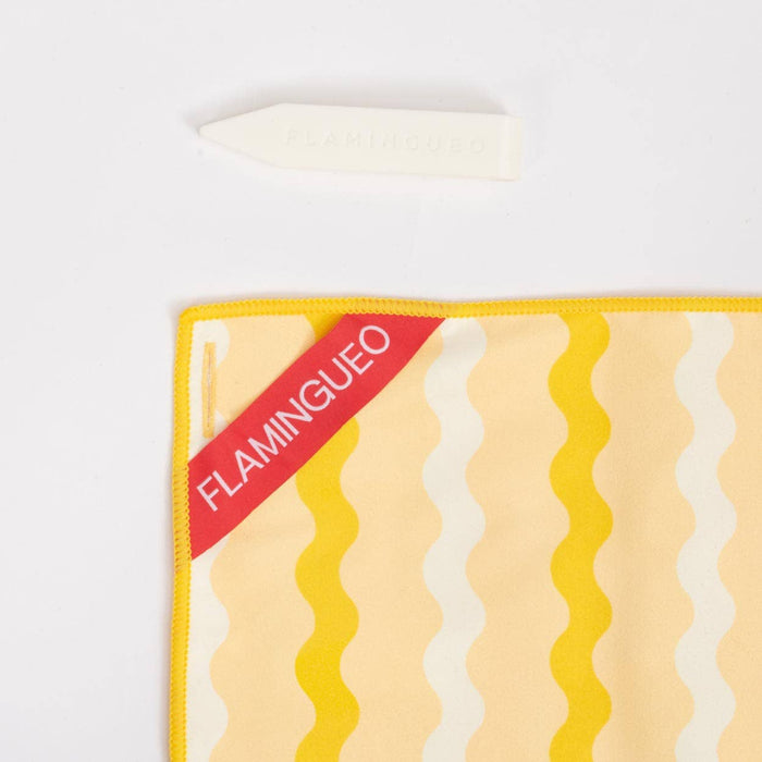 Yellow and white striped towel with 'Flamingueo' branding and cream coloured clip on a white background
