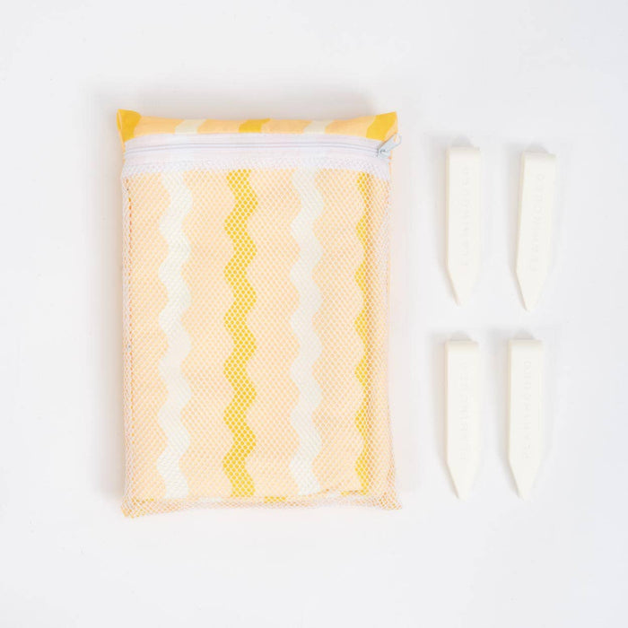Yellow and white zigzag striped towel in a white mesh pouch beside four cream coloured clips on a white background