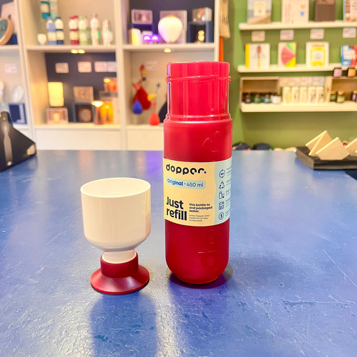 Fuchsia reusable water bottle and white cup on a blue surface with a store shelf in the background
