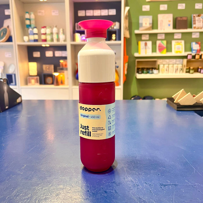 Fuchsia and white Dopper reusable water bottle with fuchsia cap on a blue surface.