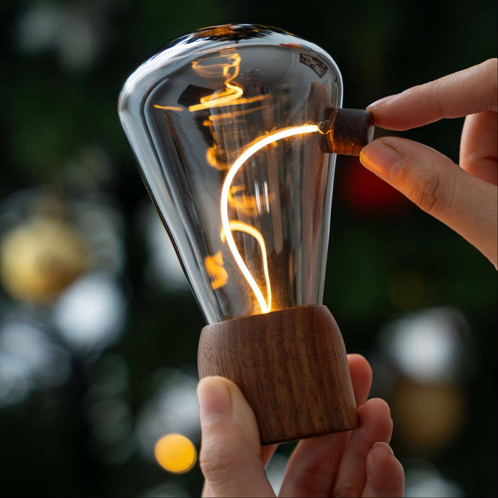 Hand holding a vintage-style light bulb with a blurred Christmas tree in the background