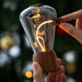 Hand holding a vintage-style light bulb with a blurred Christmas tree in the background
