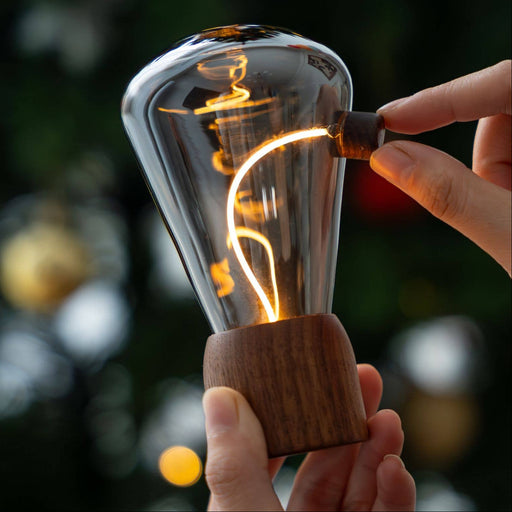 Hand holding a vintage-style light bulb with a blurred Christmas tree in the background