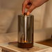 Hand touching a glass and wooden lamp on a table with a blurred background.