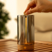 Hand placing a wooden lid on a glass lamp with a blurred background