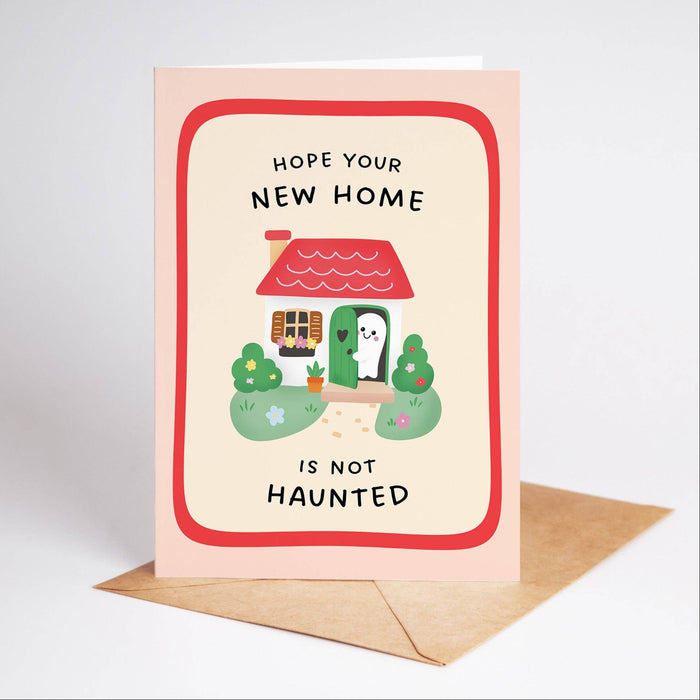 Greeting card with a cartoon house and text 'Hope your new home is not haunted' on a light pink background.