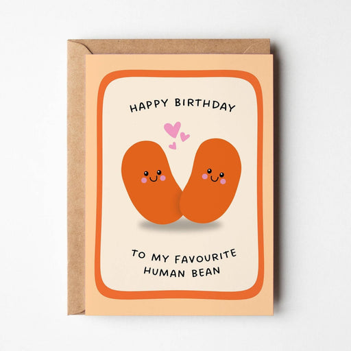 A funny birthday card with a kraft envelope, featuring a cute illustration of two smiling human beans on a peach card front with the text 'HAPPY BIRTHDAY TO MY FAVOURITE HUMAN BEAN'.