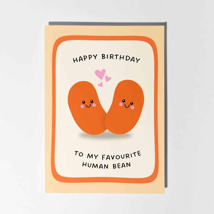 A cute birthday card featuring two smiling orange human beans with small pink hearts above them. The text reads 'HAPPY BIRTHDAY TO MY FAVOURITE HUMAN BEAN'.