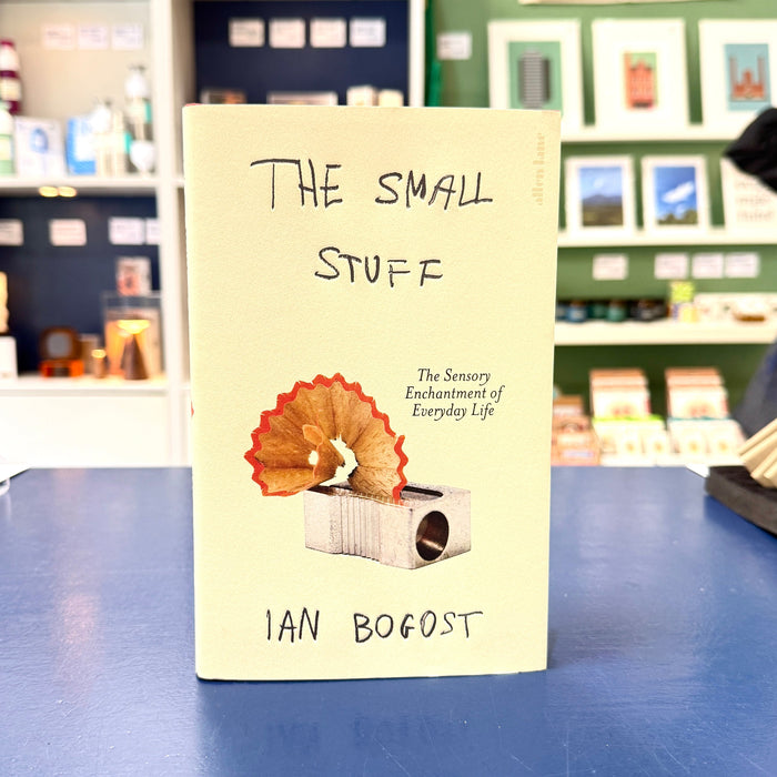 The Small Stuff book by Ian Bogost standing upright on a blue table in a store setting, with its cream-colored cover showing a pencil sharpener illustration and handwritten-style title text.