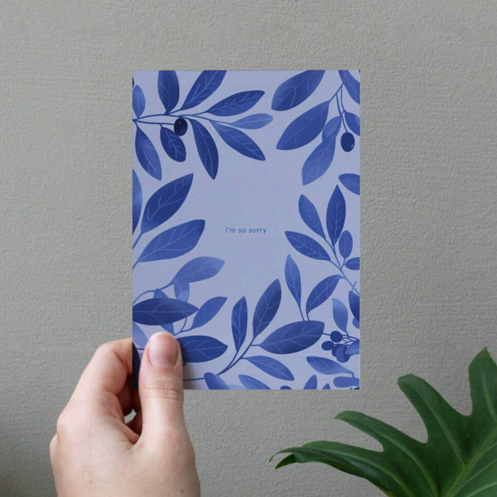 Hand holding a card with blue leaf pattern against a gray wall