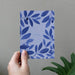 Hand holding a card with blue leaf pattern against a gray wall