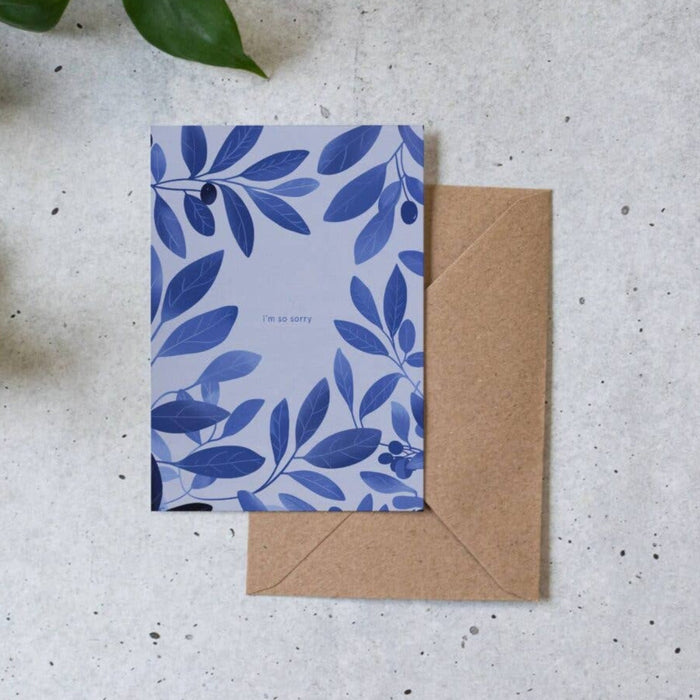 Blue floral card with a brown envelope on a textured surface with green leaves.