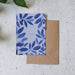 Blue floral card with a brown envelope on a textured surface with green leaves.