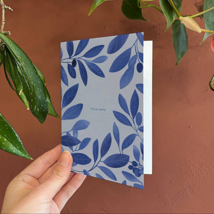 Hand holding a blue floral-patterned card against a brown background with green leaves.
