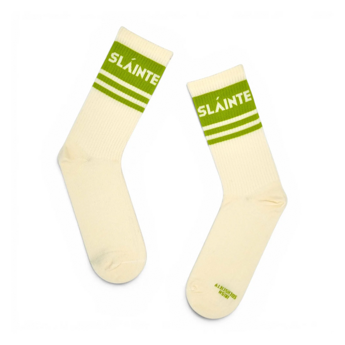 A pair of off-white crew socks with green stripes and the word 'SLÁINTE' printed in white on the ribbed cuffs, displayed against a plain white background.