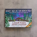 A jigsaw puzzle advent calendar titled 'Night Out at the North Pole' resting on a textured gray surface. The box features a colorful winter night scene with aurora lights, a bridge, and snowy trees, with text indicating 24 jigsaw puzzles in 1 big picture.