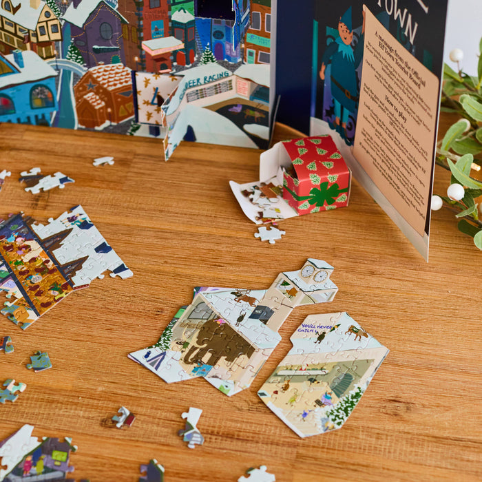 A jigsaw puzzle set displayed on a wooden table, with scattered puzzle pieces, a small bowl of mixed nuts, and a colorful illustrated puzzle box and sign in the background.