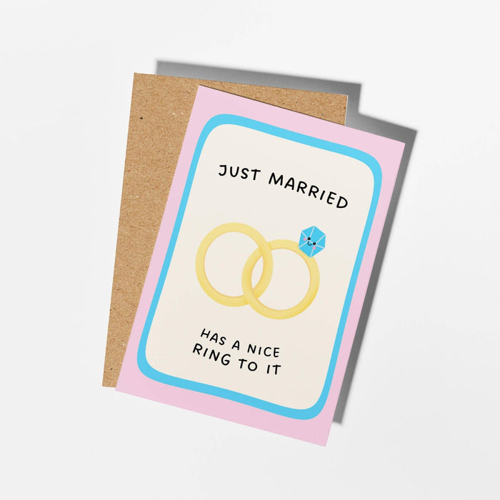 A square greeting card with a kraft paper backing, featuring a pastel design with the text 'JUST MARRIED HAS A NICE RING TO IT' and an illustration of two interlocking rings.