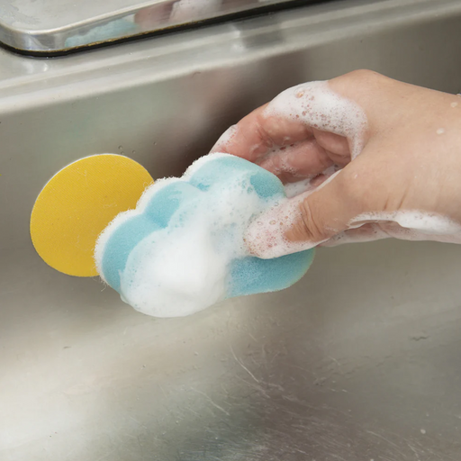 Hand holding a blue sponge with soap suds over a sink.