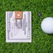 Fifty dollar bill with steel and wood money clip and golf ball on a grass surface.