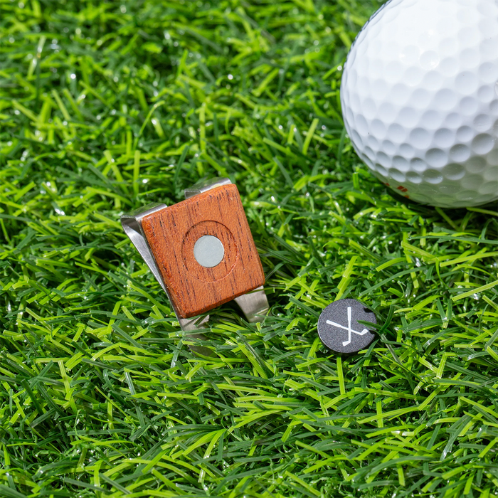 Golf divet tool, ball marker, and golf ball on grass surface.