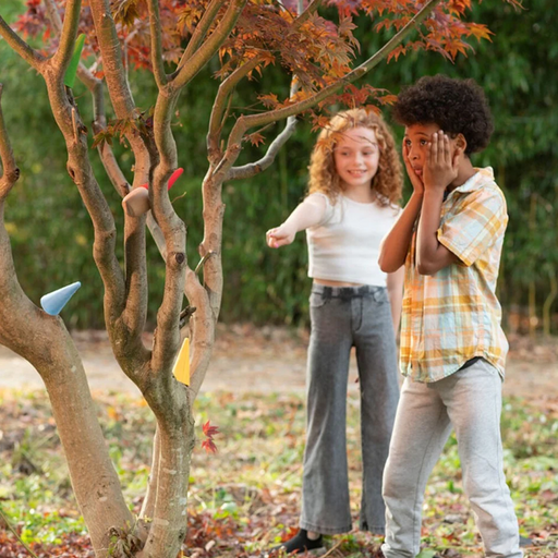 Two children standing in a garden with trees with small gnome hats.