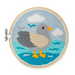A circular embroidery hoop containing a stylized seagull stitched in gray, beige, turquoise, and yellow thread, with white clouds in a light blue sky, shown on a white background.