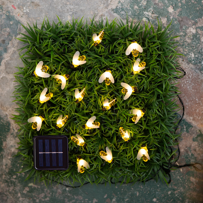 Solar-powered bee string lights on a green grass-like mat.