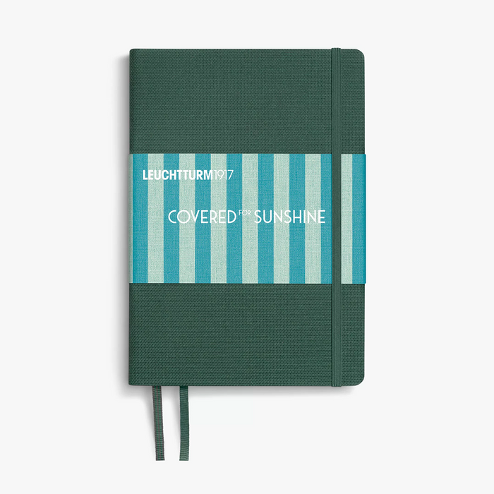 A Leuchtturm1917 notebook with a dark green textured cover, a blue and white striped paper band labeled 'COVERED IN SUNSHINE', and matching green ribbon bookmarks, shown on a light gray background.