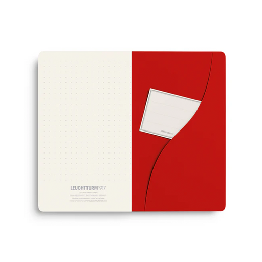A Leuchtturm1917 notebook shown open, with an off-white dotted left page and a bold red right pocket holding a white card, on a light gray background.