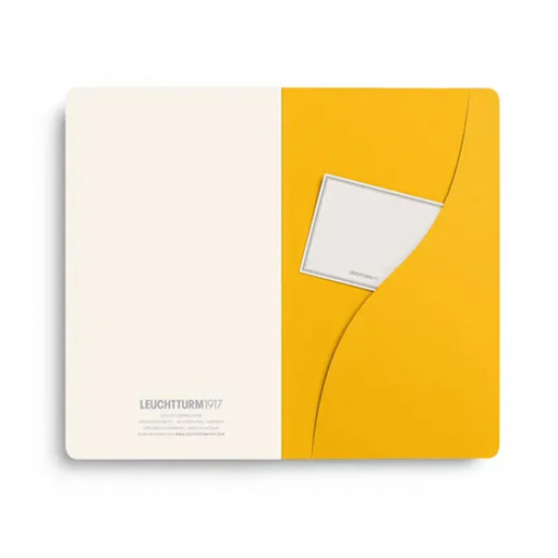 A Leuchtturm1917 notebook laying open: one half is warm off-white and the other is bright yellow, featuring a small white envelope pocket on the yellow side.