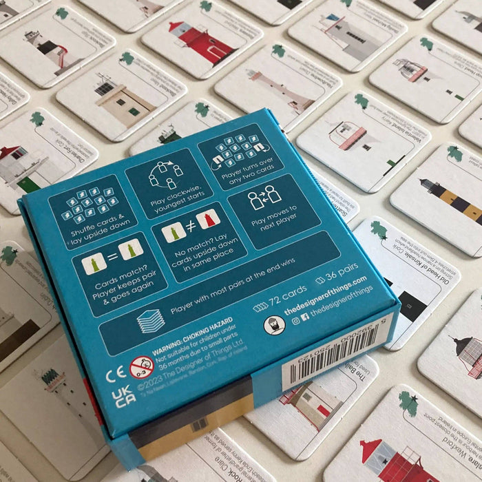 Rear of card game packaging on top of game cards featuring illustrations of lighthouses on a light surface.